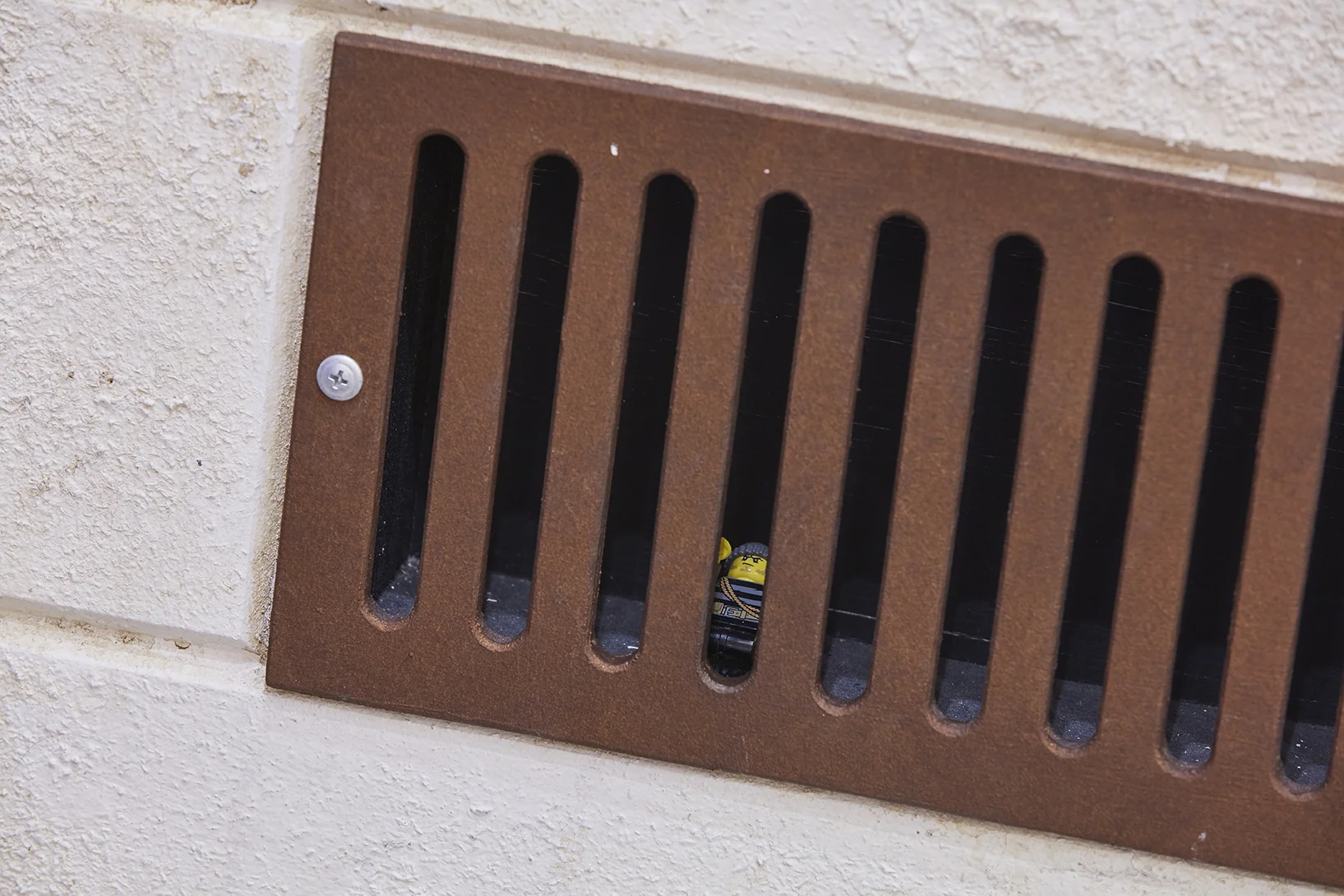 Close up of wall grate with small LEGO burglar man trapped inside