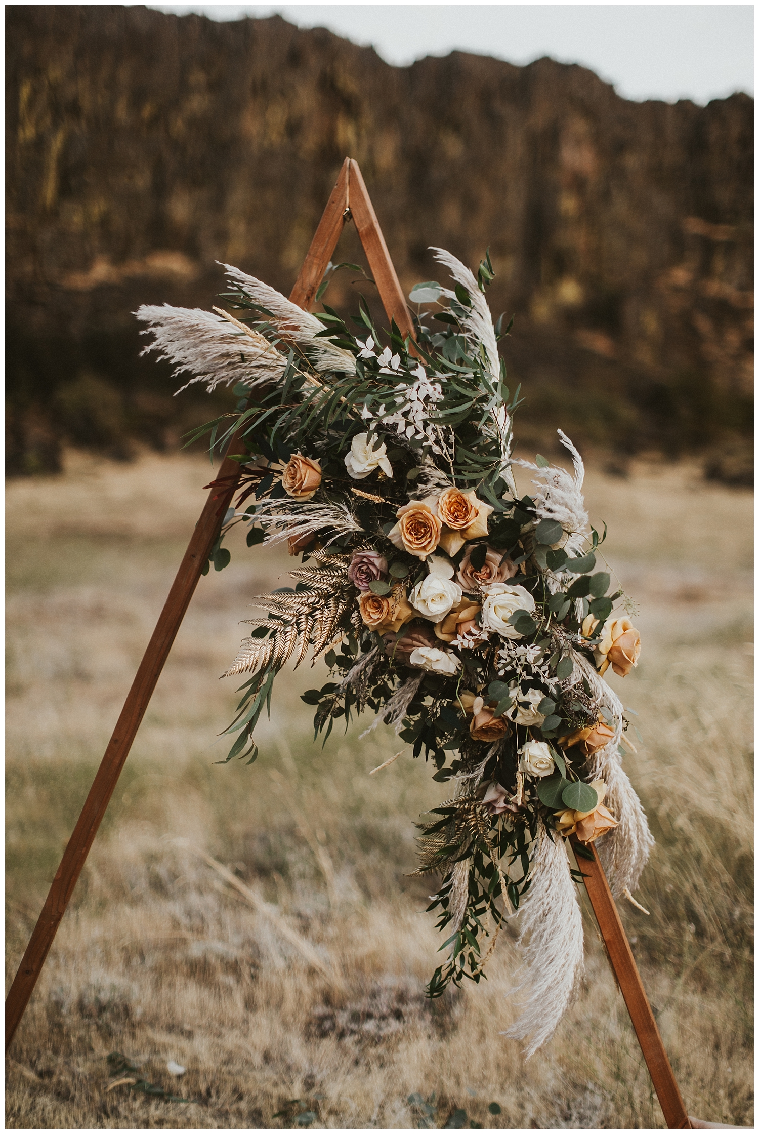 a wooden triangle arch with dried leaves and beautiful boho flowers