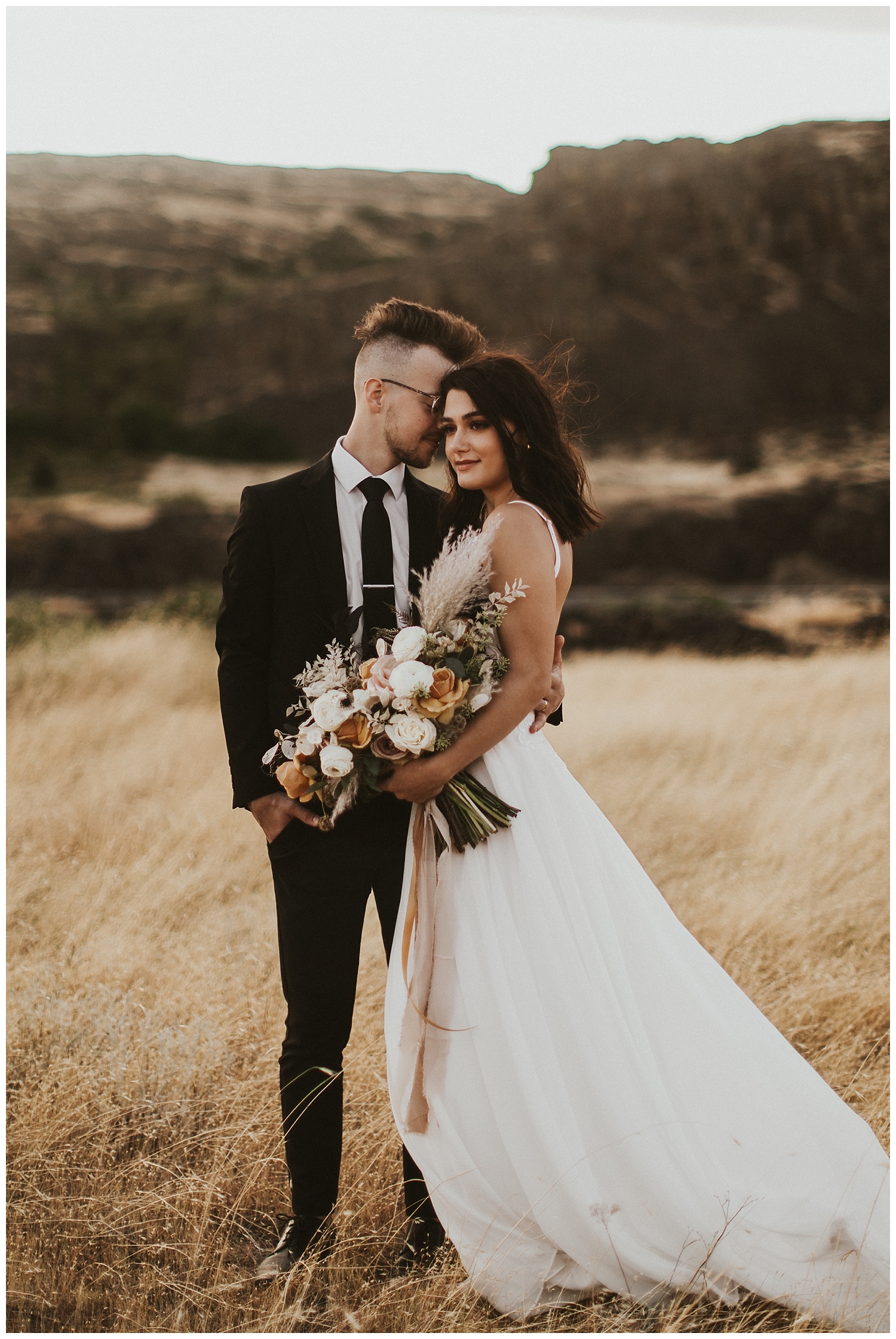 groom nuzzles his bride's ear as she look into the distance, her wedding dress blowing in the wind