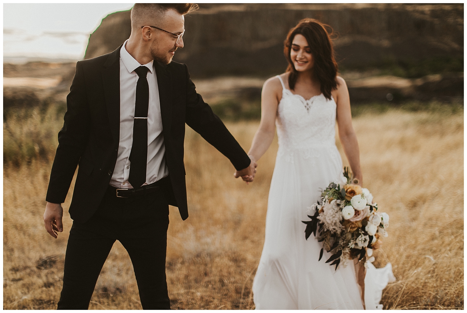 a bride and groom walk hand in hand in the desert