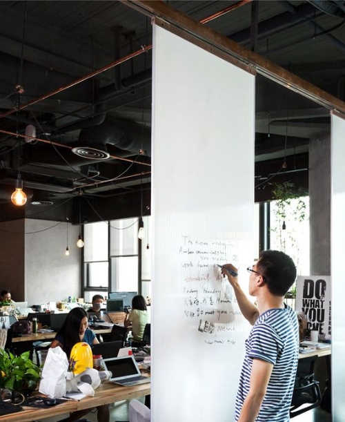 Man writing on white board while colleagues work around him