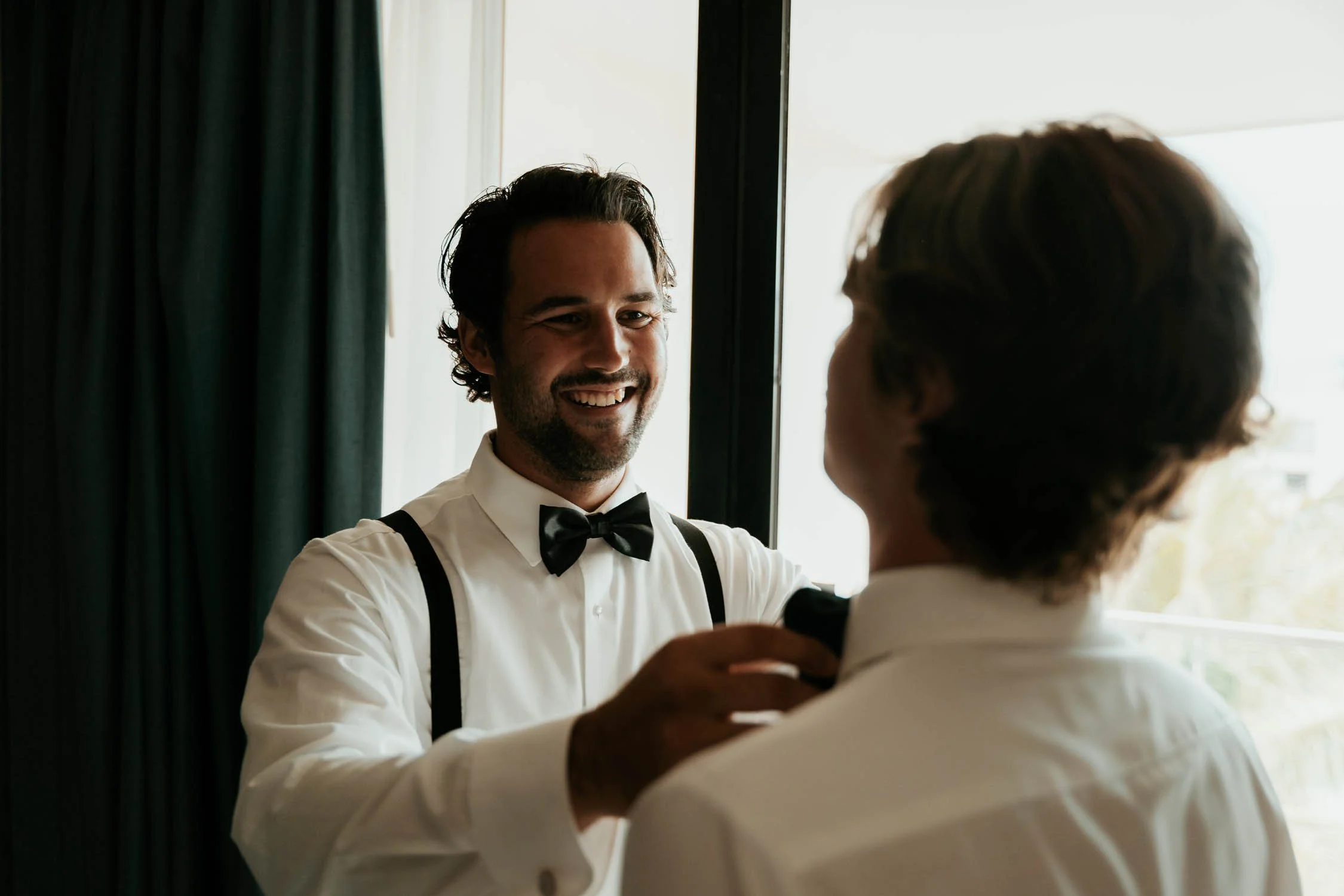 bestman helping the groom getting ready close to a window
