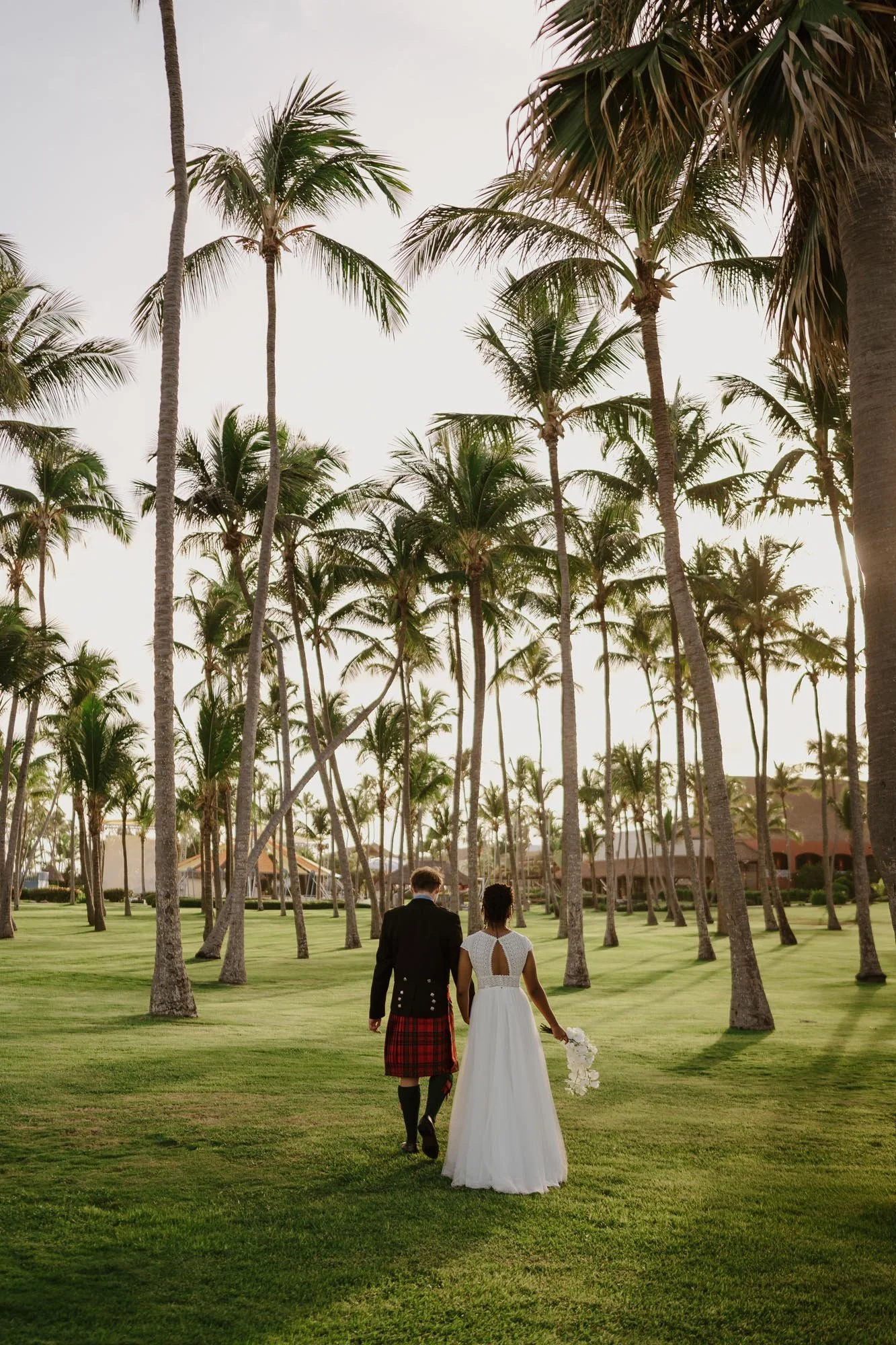 Bride and groom in kilts walking down the sunset and palm tress in chez bisutti wedding punta cana