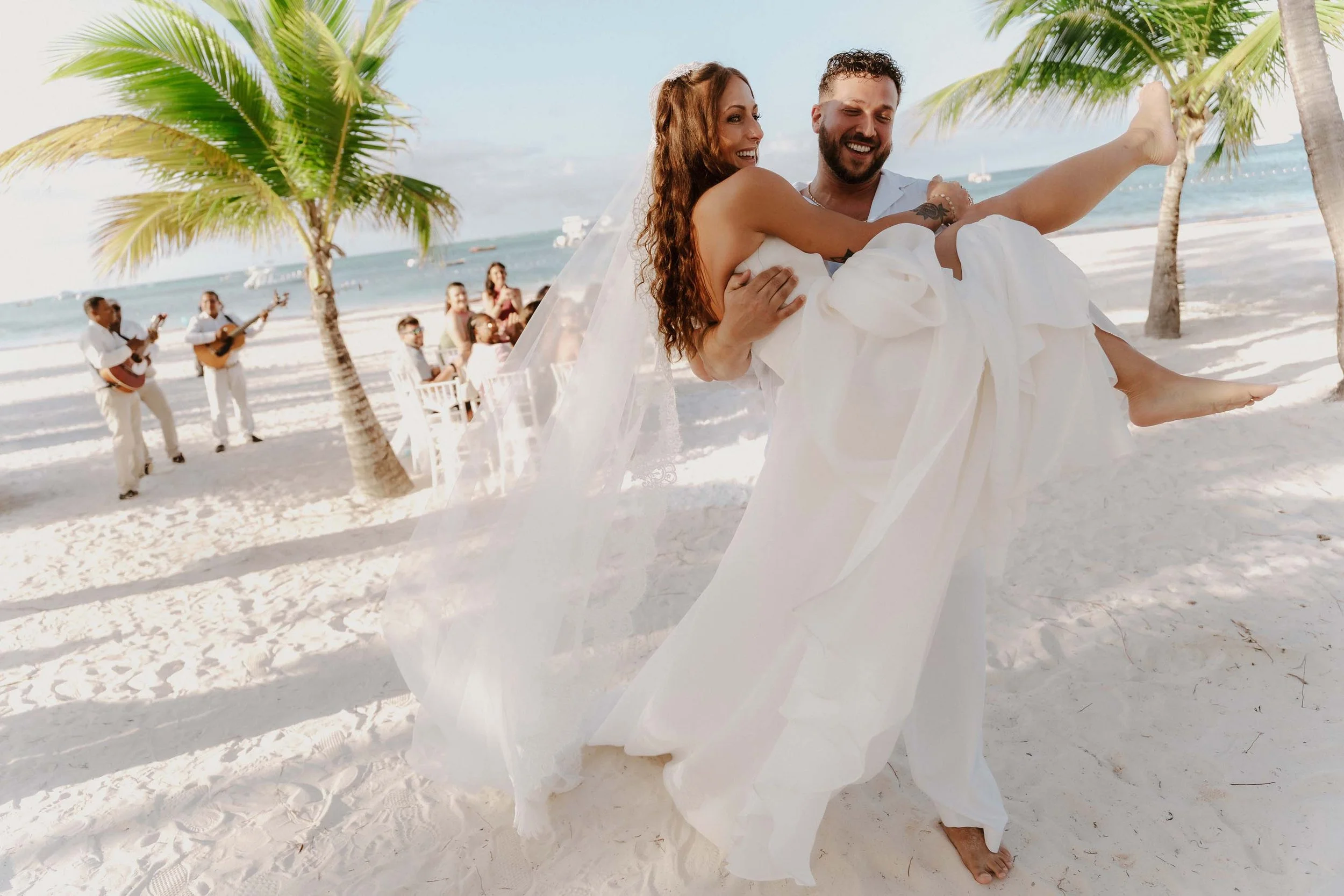 Bride and groom walking down the aisle as husband and wife while the groom picks and holds the bride in his arm walking down the aisle barefoot in the sand