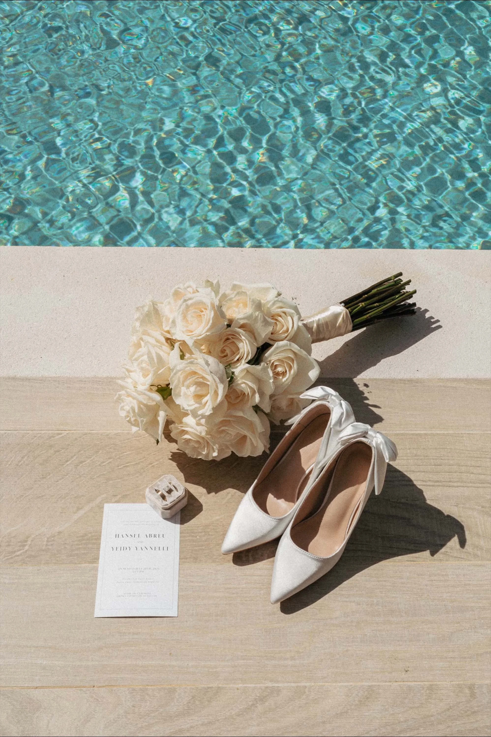 Shoes, flower, rings and invitations close to the pool