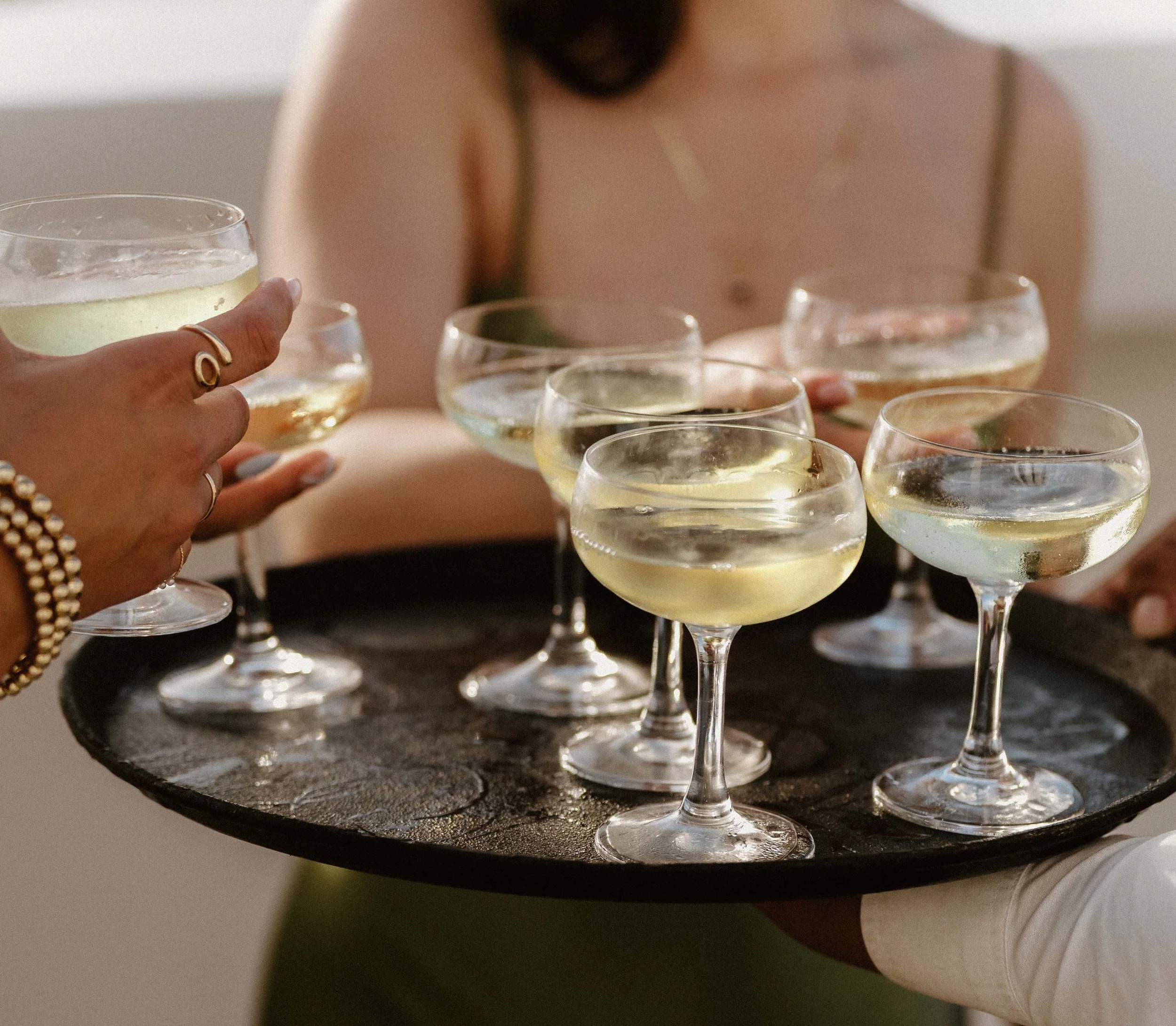 A warm, editorial close-up of a guest reaching for a champagne coupe glass from a tray during an elegant destination wedding cocktail hour in Cap Cana Punta Cana.