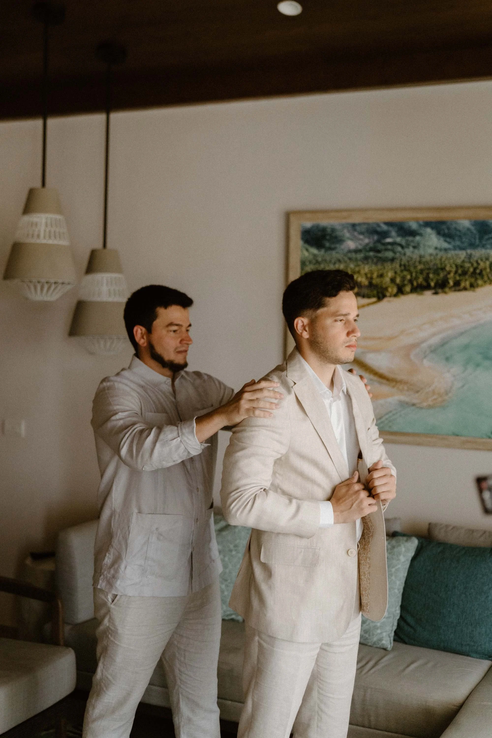 A candid, editorial moment of the groom getting ready in a crisp linen suit, being helped by his best man before his destination wedding in Cap Cana Punta Cana