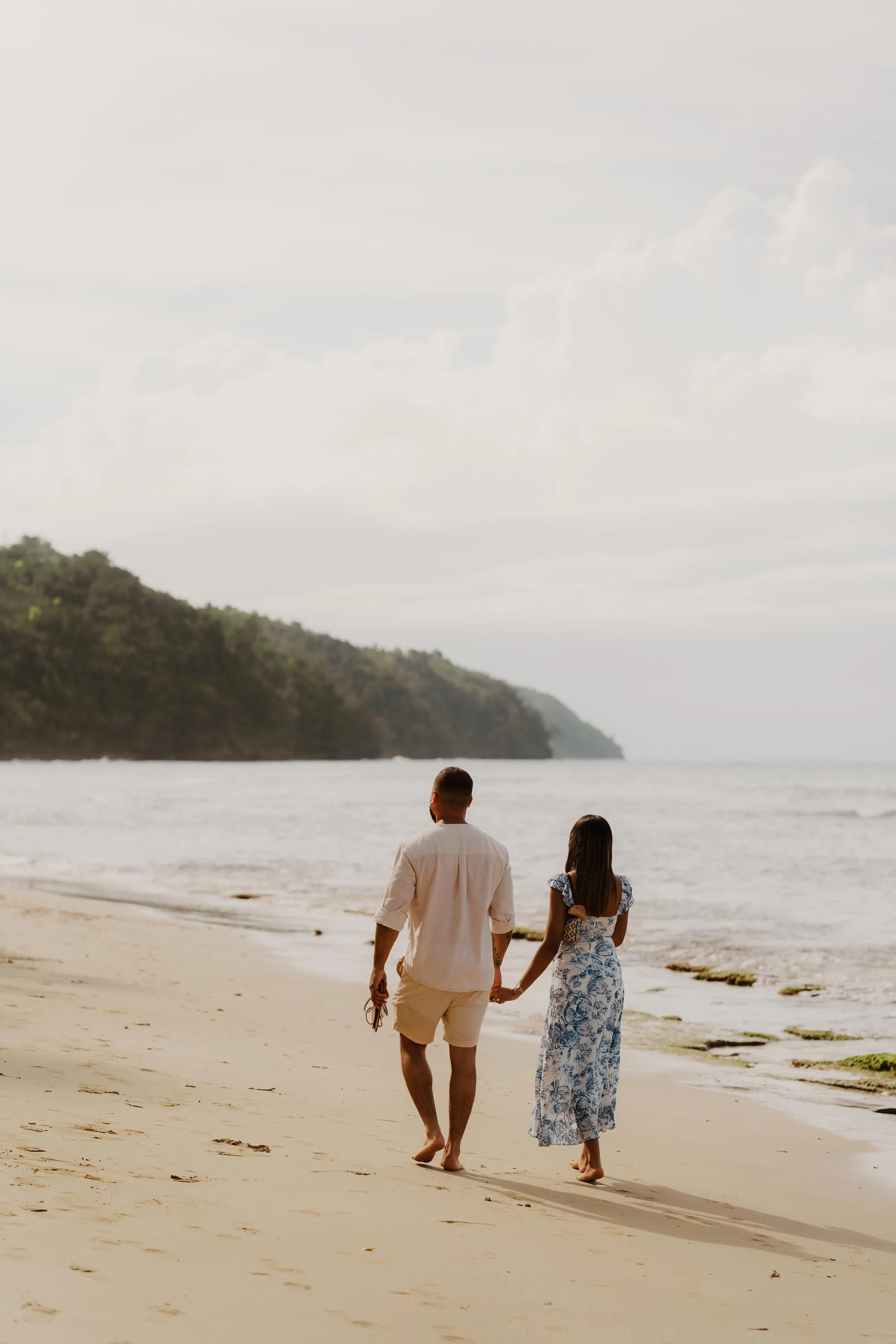 Couple walking down the beach while holding hands, in the background you can see the mountains and the tropical forest in Samana