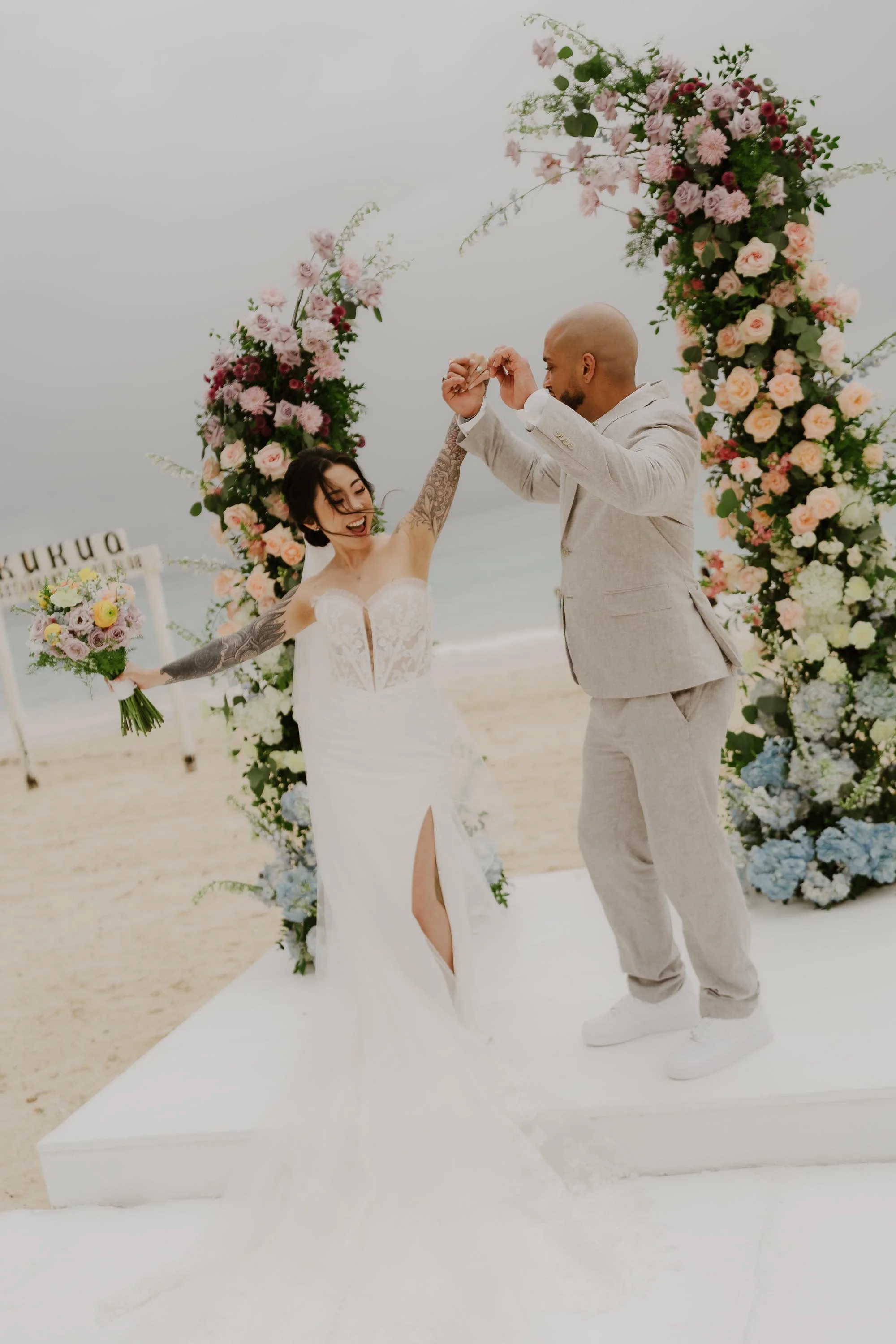 Candid moment of a bride and groom joyfully dancing between pastel floral pillars at their Kukua Beach Club wedding on Bavaro Beach, Punta Cana.