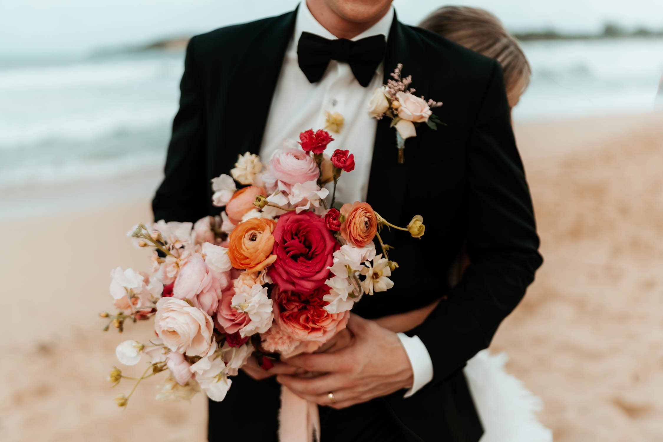 bride huging the groom while holding a colorfull wedding bouquet