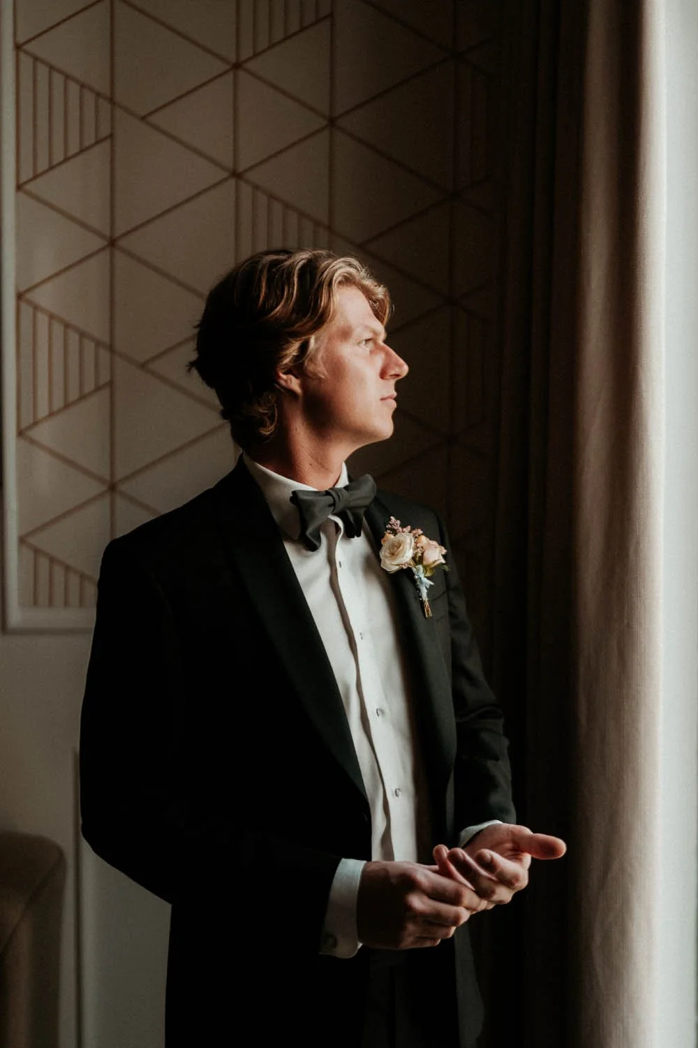 Groom getting ready for his wedding close to a window
