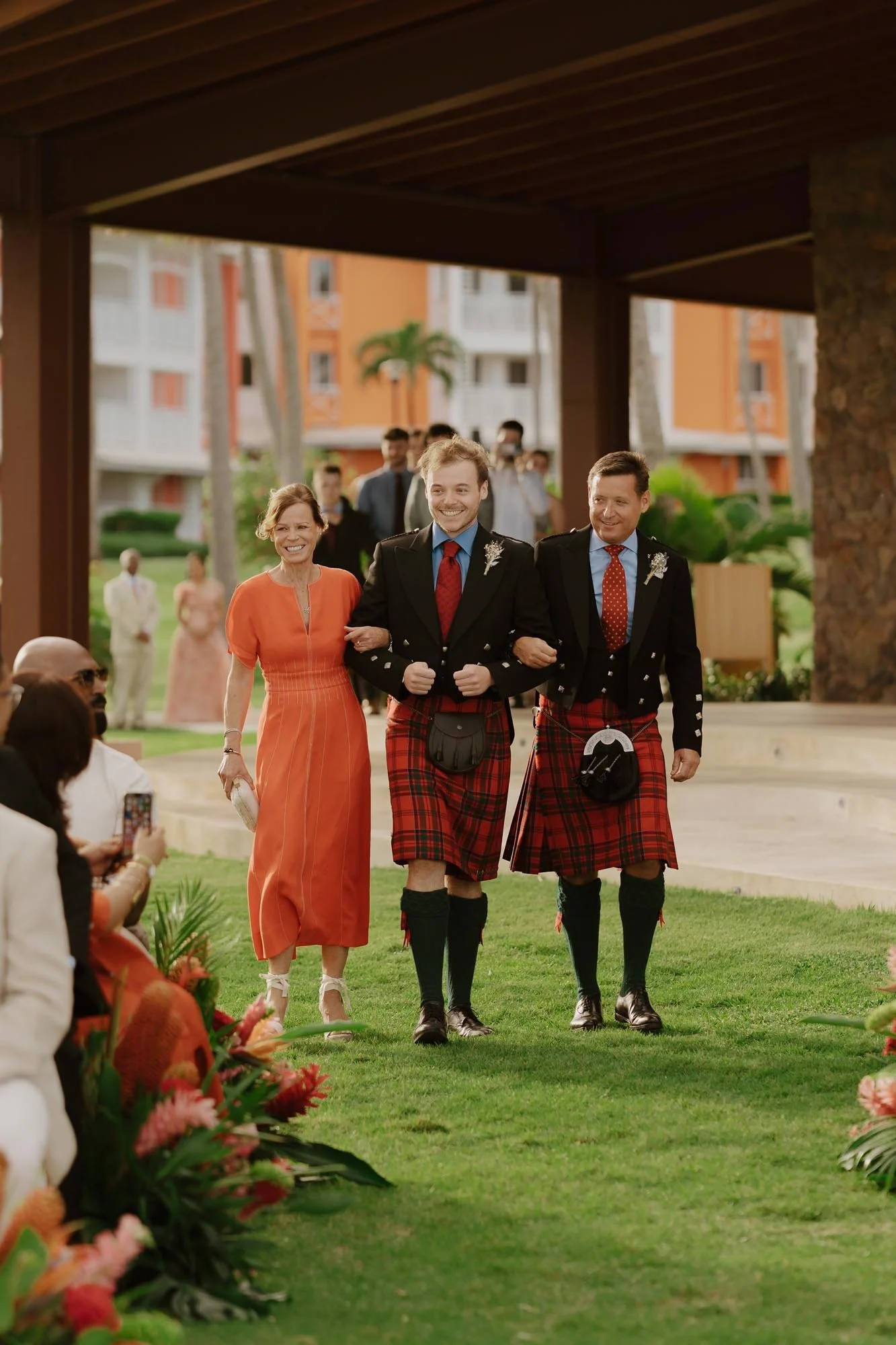 Groom walking with his mom and dad wearing kilts in the way to the aisle of the ceremony close to the beach and the ceremony in Punta Cana Dominican Republic Chez Bisutti