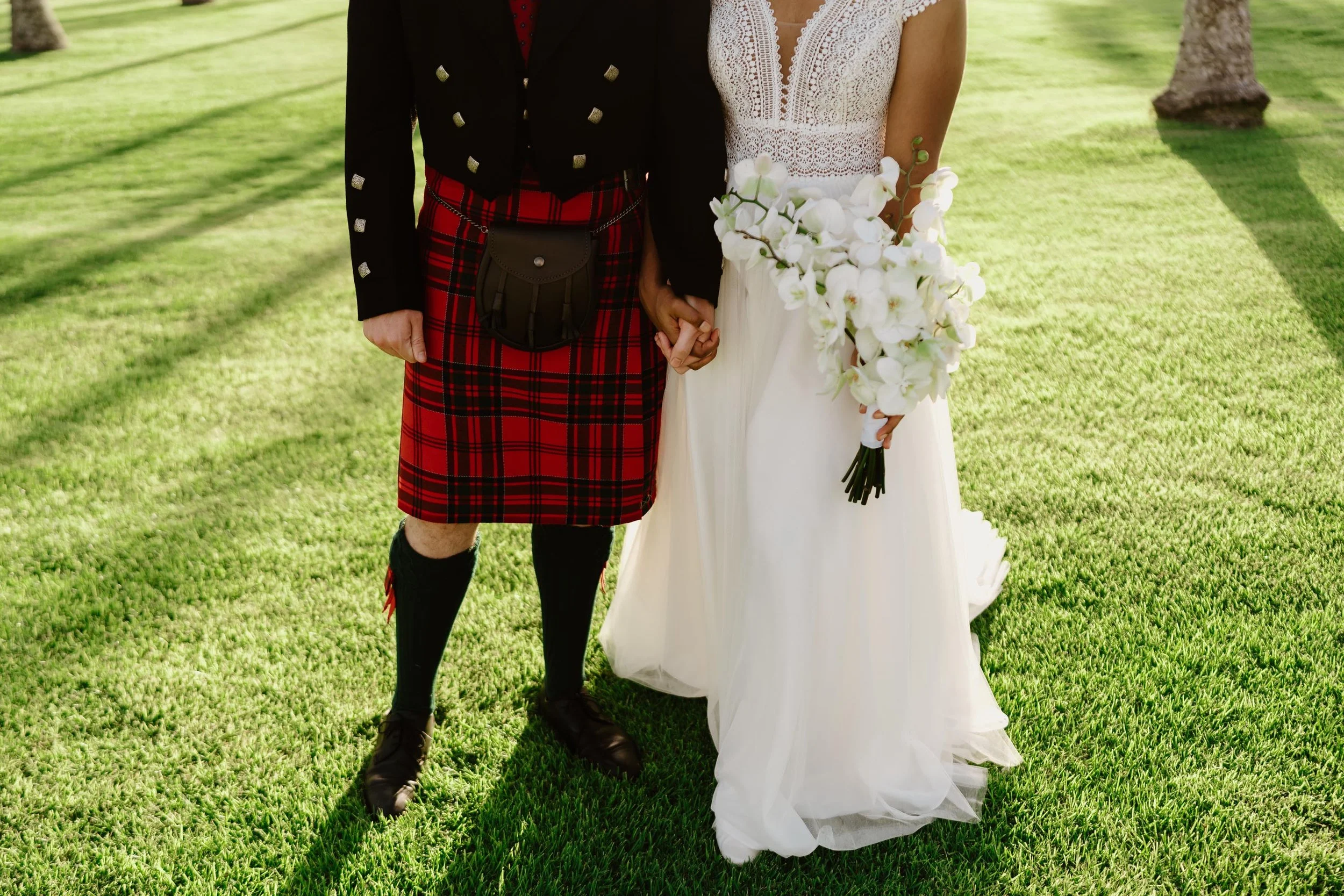 Bride ang groom with kilts holding hands after ceremony in green grass in Chez Bisutti
