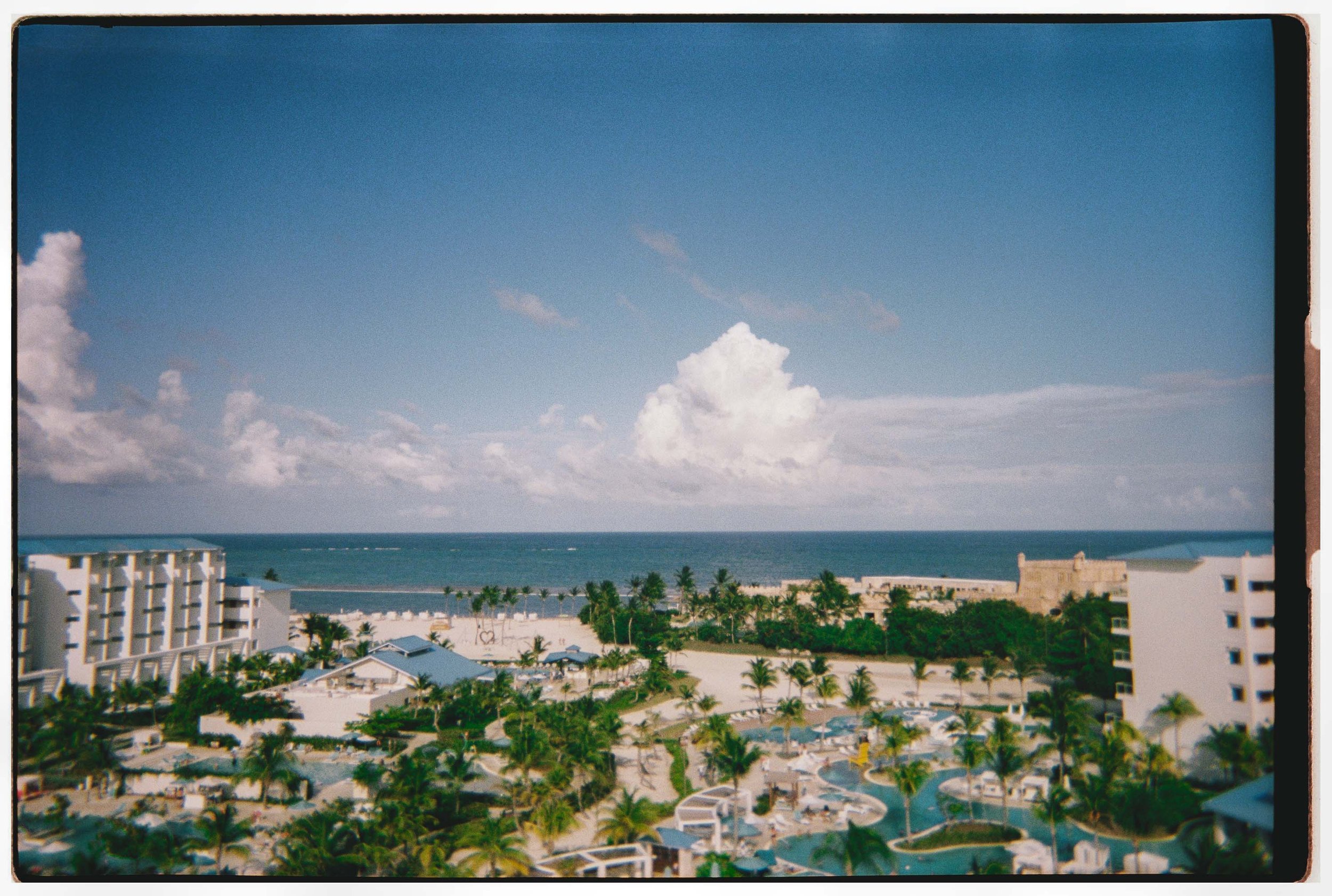 A nostalgic, film-inspired landscape shot of the serene oceanfront resort and bright blue Caribbean sky, setting the perfect scene for a destination wedding in Cap Cana Punta Cana