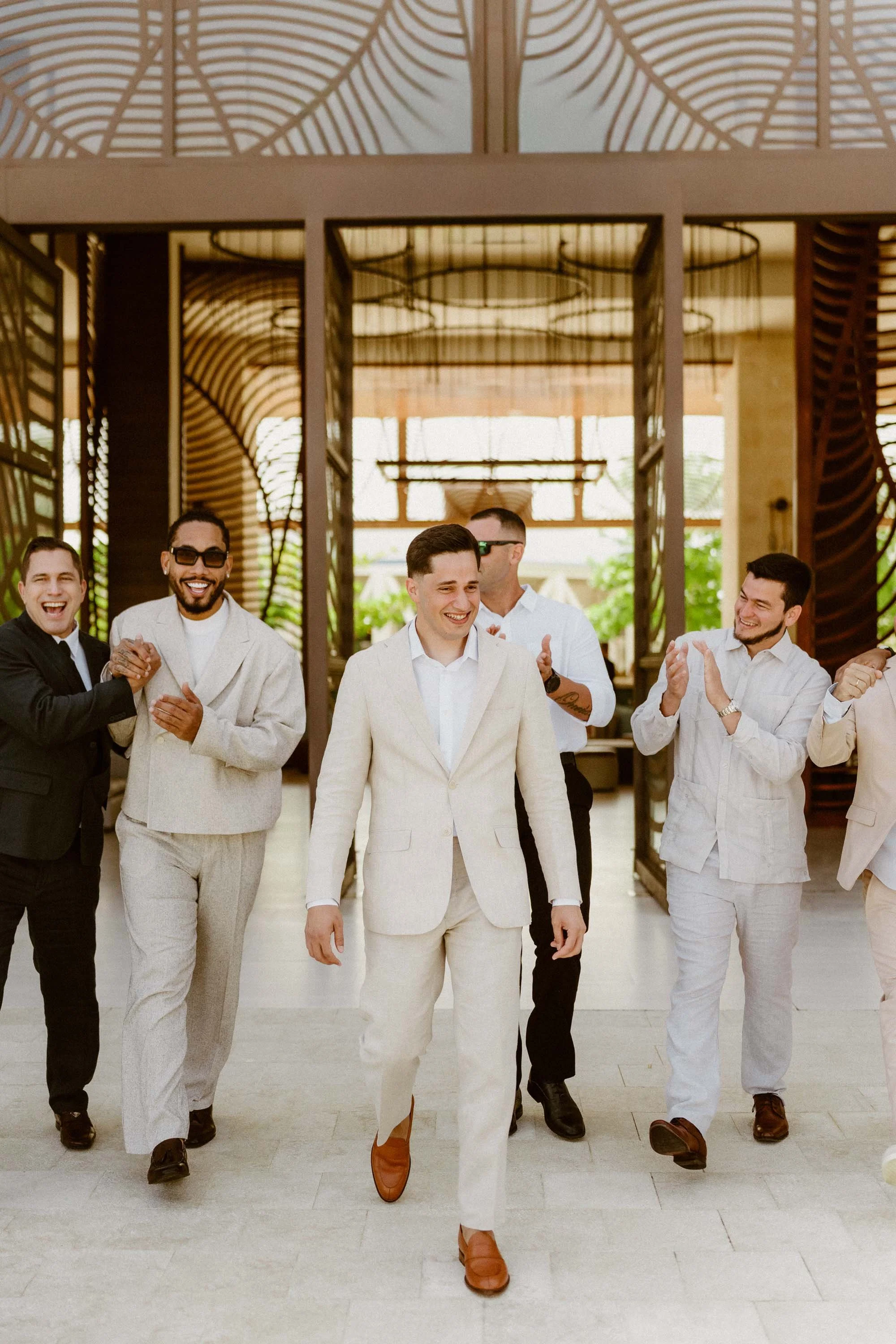 Candid photo of a joyful groom in a light linen suit walking and laughing with his groomsmen before the wedding ceremony at a luxury resort in Cap Cana Punta Cana