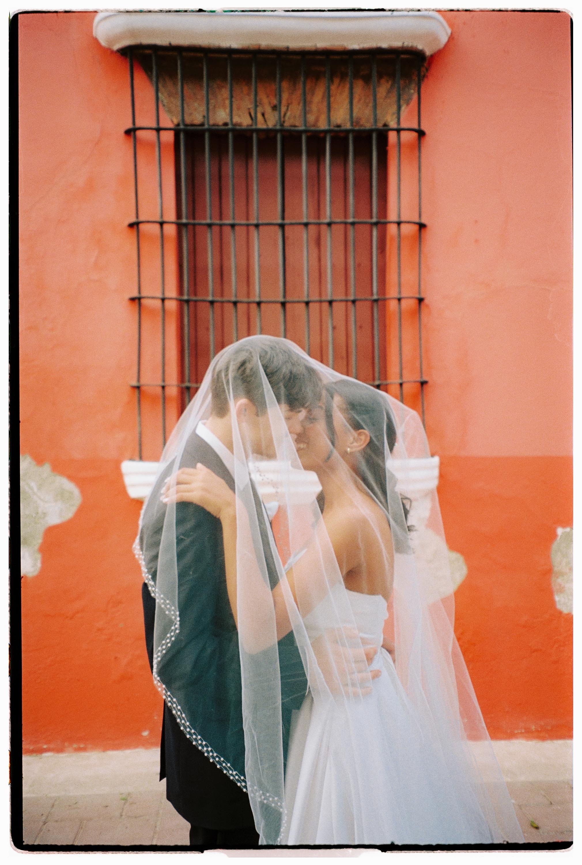 Bride and groom under a veil in front of a terracotta colonial wall in the Zona Colonial.