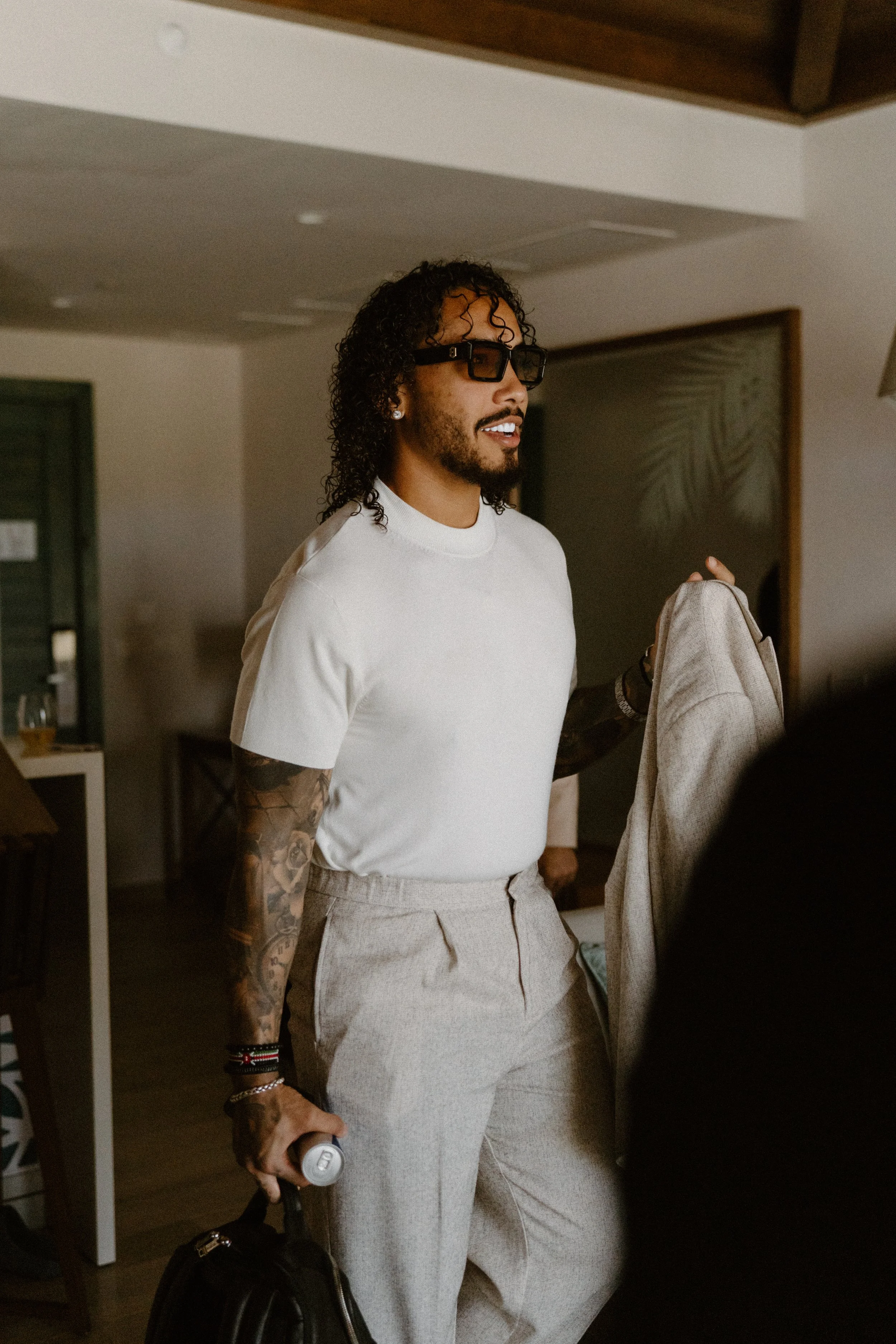Candid, editorial portrait of a stylish groomsman holding his linen jacket and smiling naturally during the relaxed morning wedding prep in Cap Cana Punta Cana