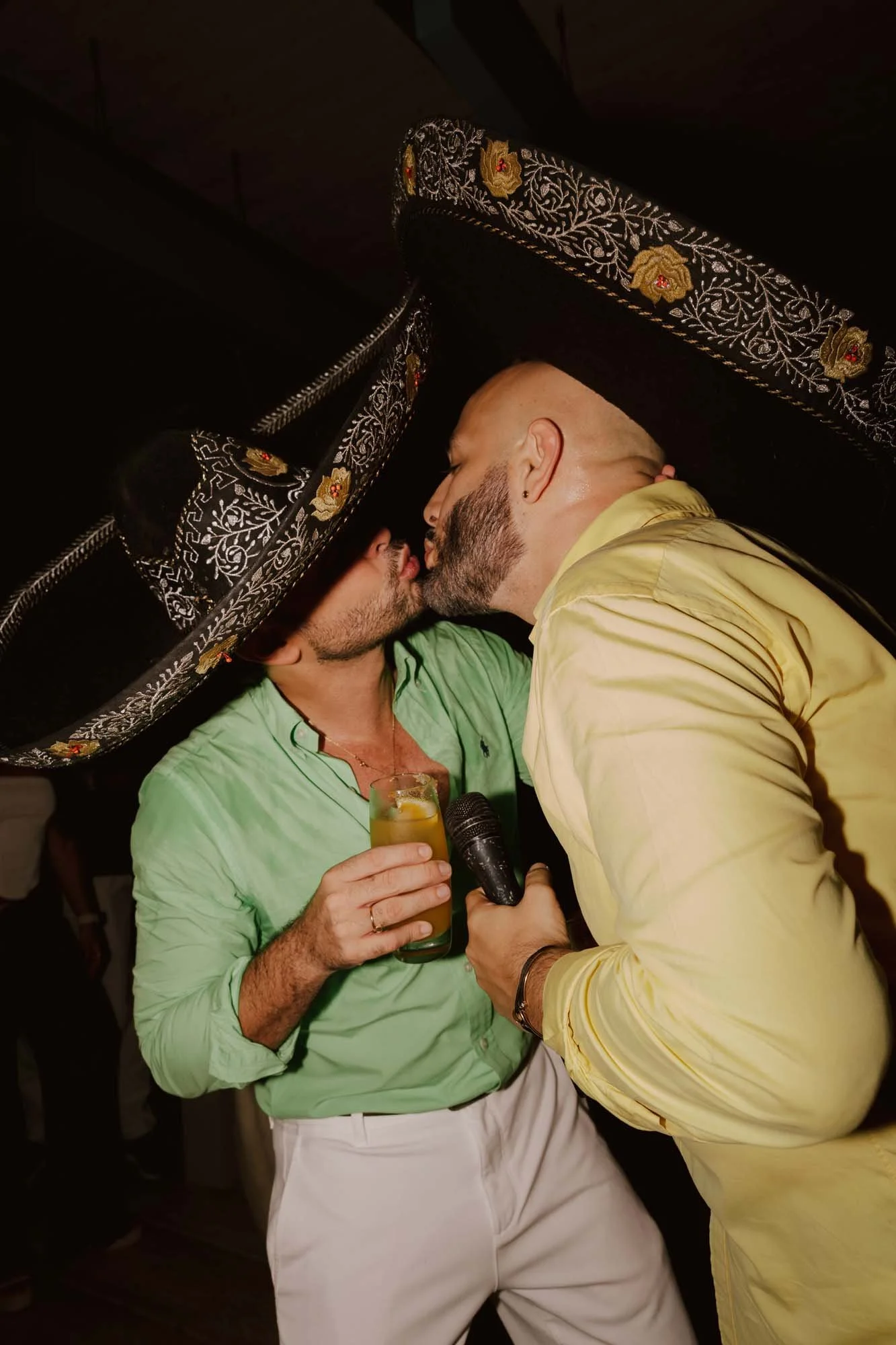 Same sex couple, two grooms about to kiss while they wear traditional Mexican hats