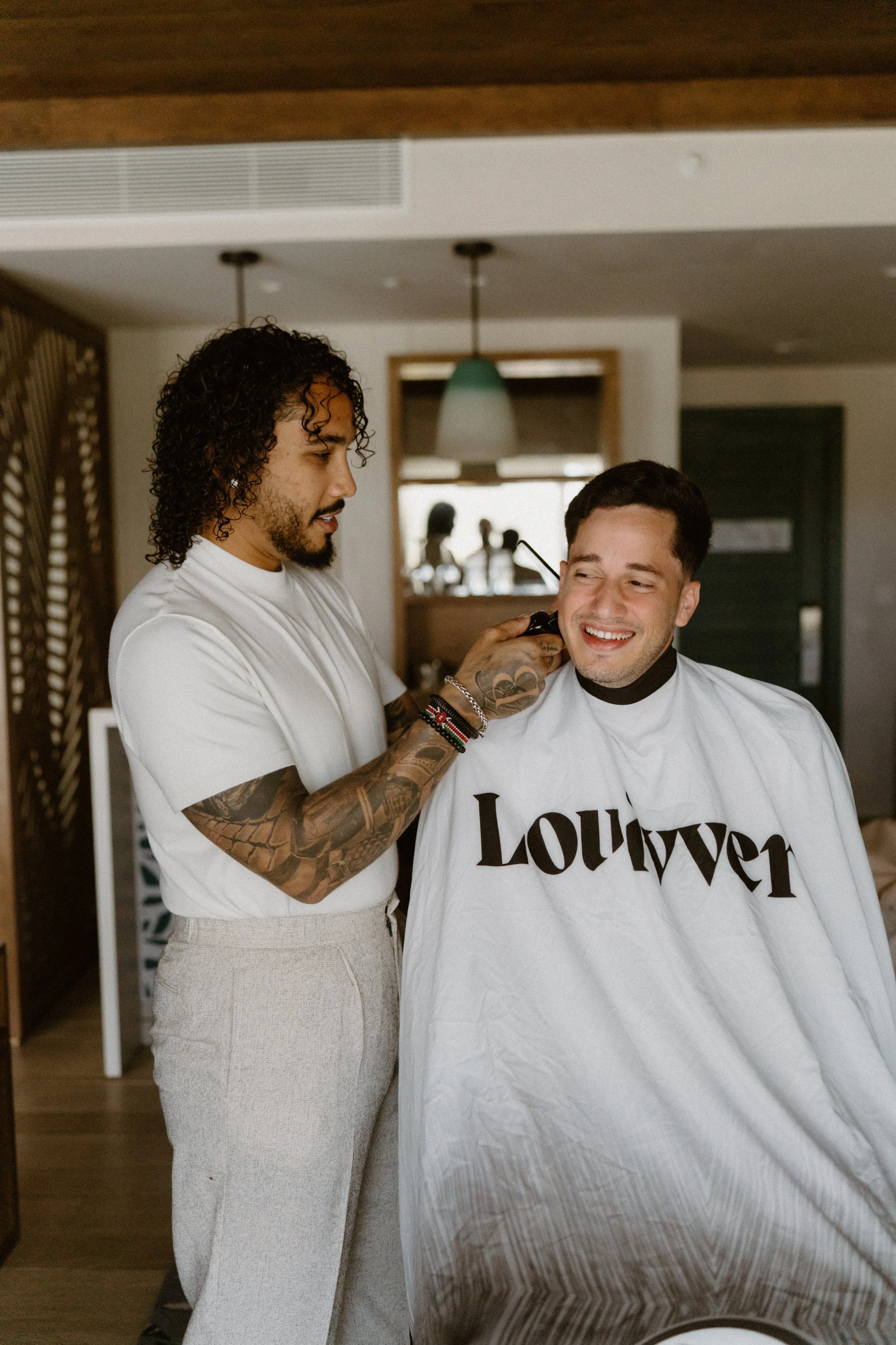 A candid, storytelling moment of the groom sharing a laugh while getting a fresh haircut from his best friend during the wedding morning preparations in Cap Cana Punta Cana