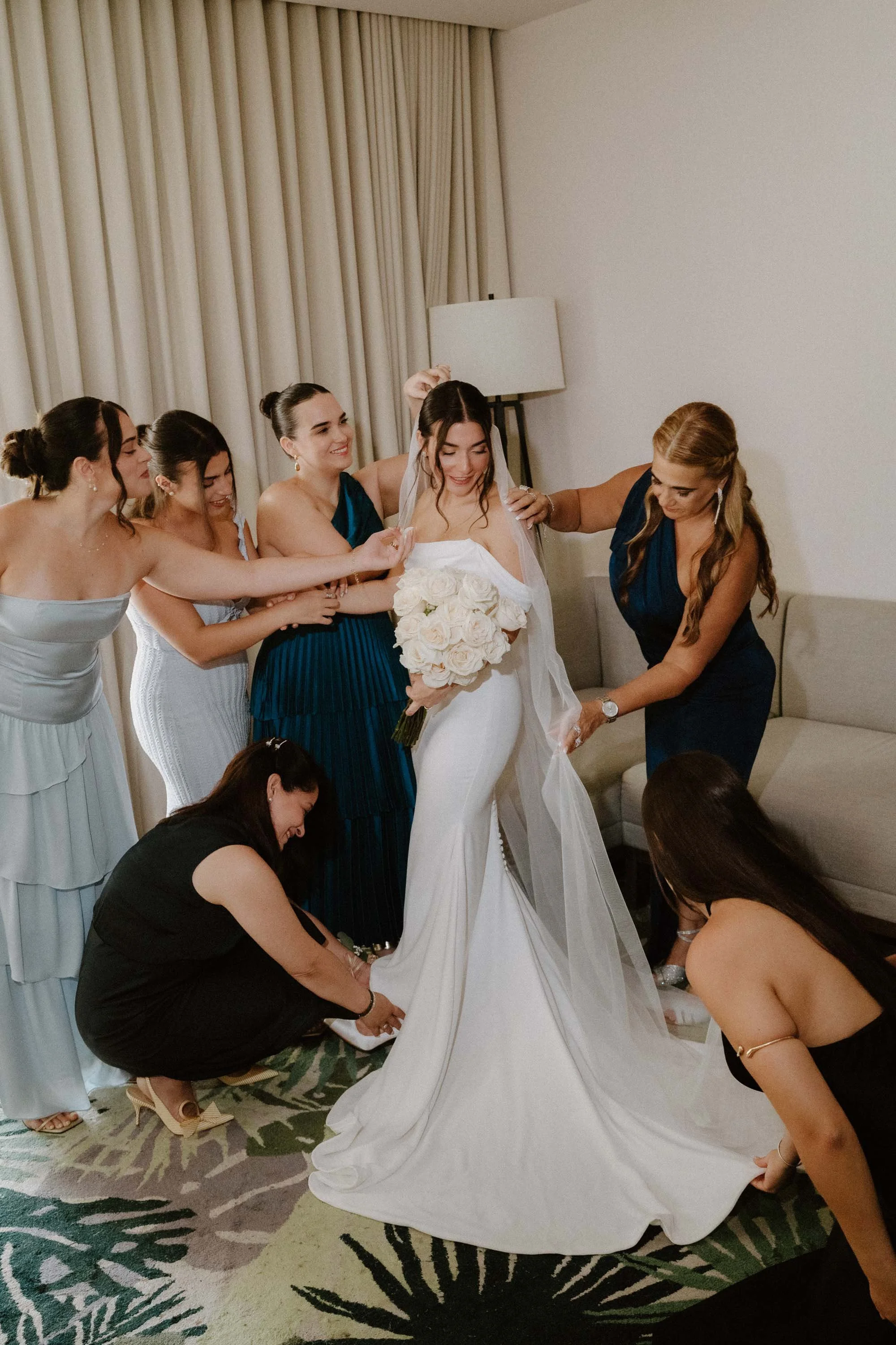 Bridemaids and mom helping the bride get ready and fully dress in the room