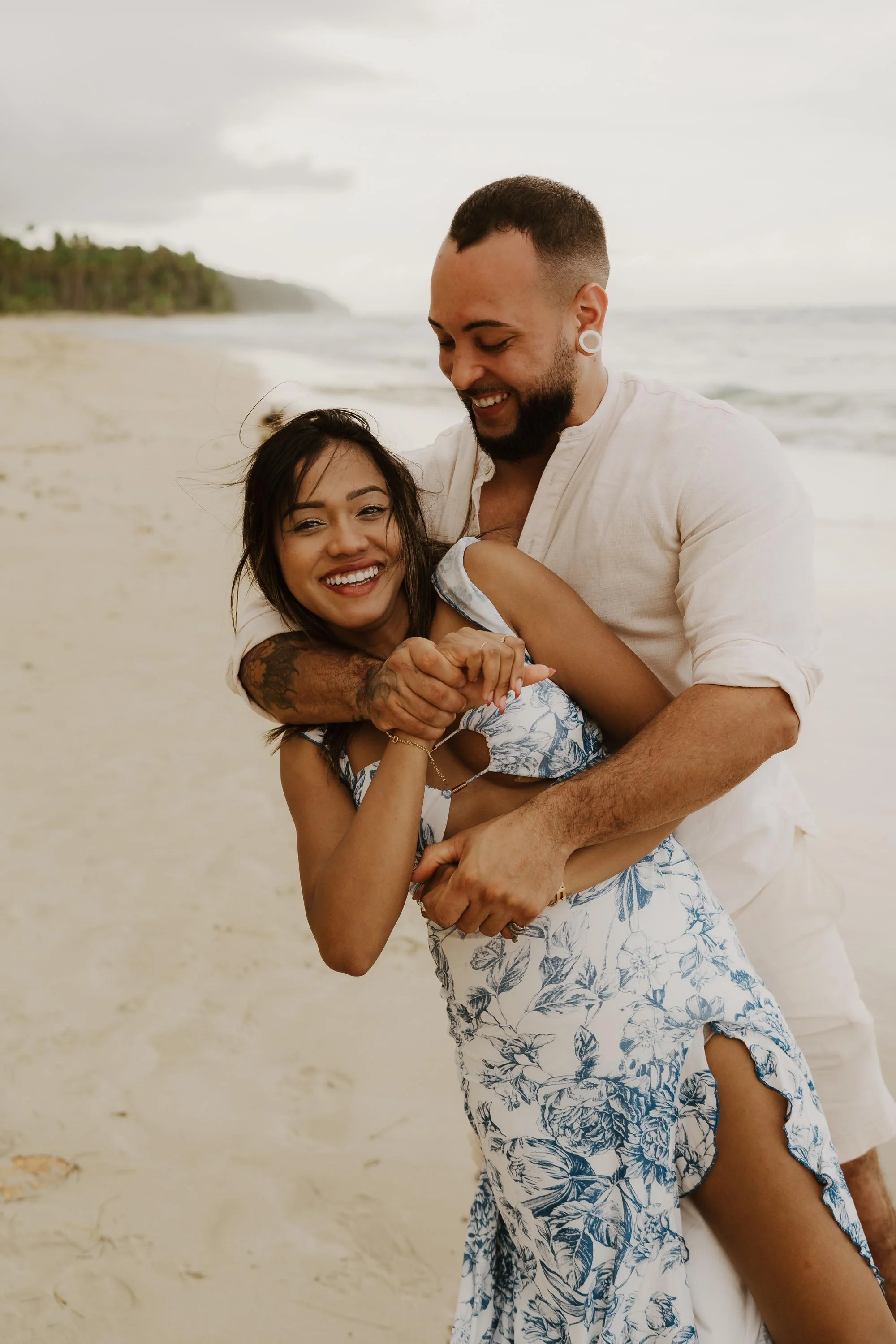 Candid portrait of couple in the beach of Samana holding each other and laughing with the beach in the background
