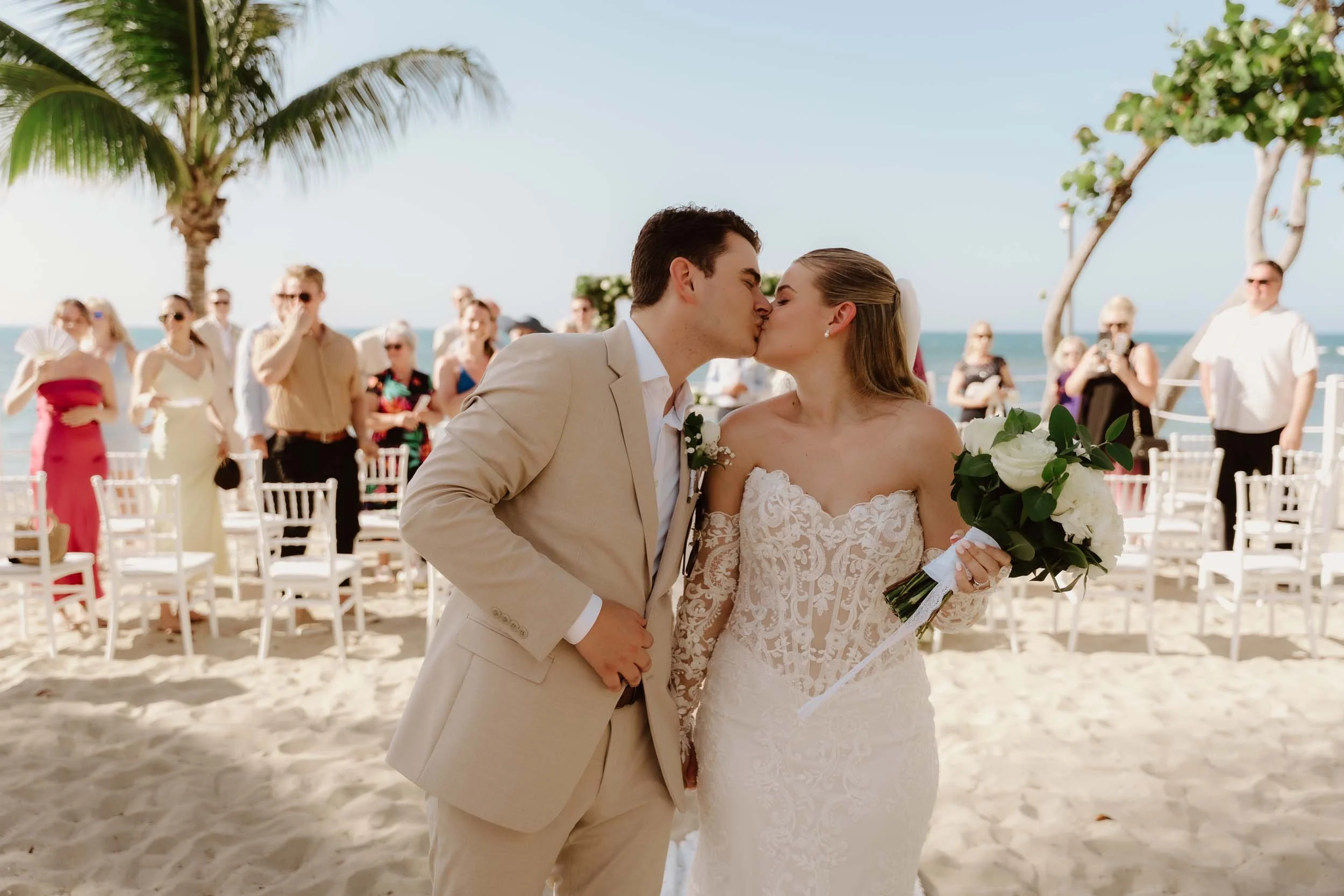 Bride and groom kissing while they walk down the aisle. You can see the guest in the backgruond and the beach and the palms tree in Puerto Plata