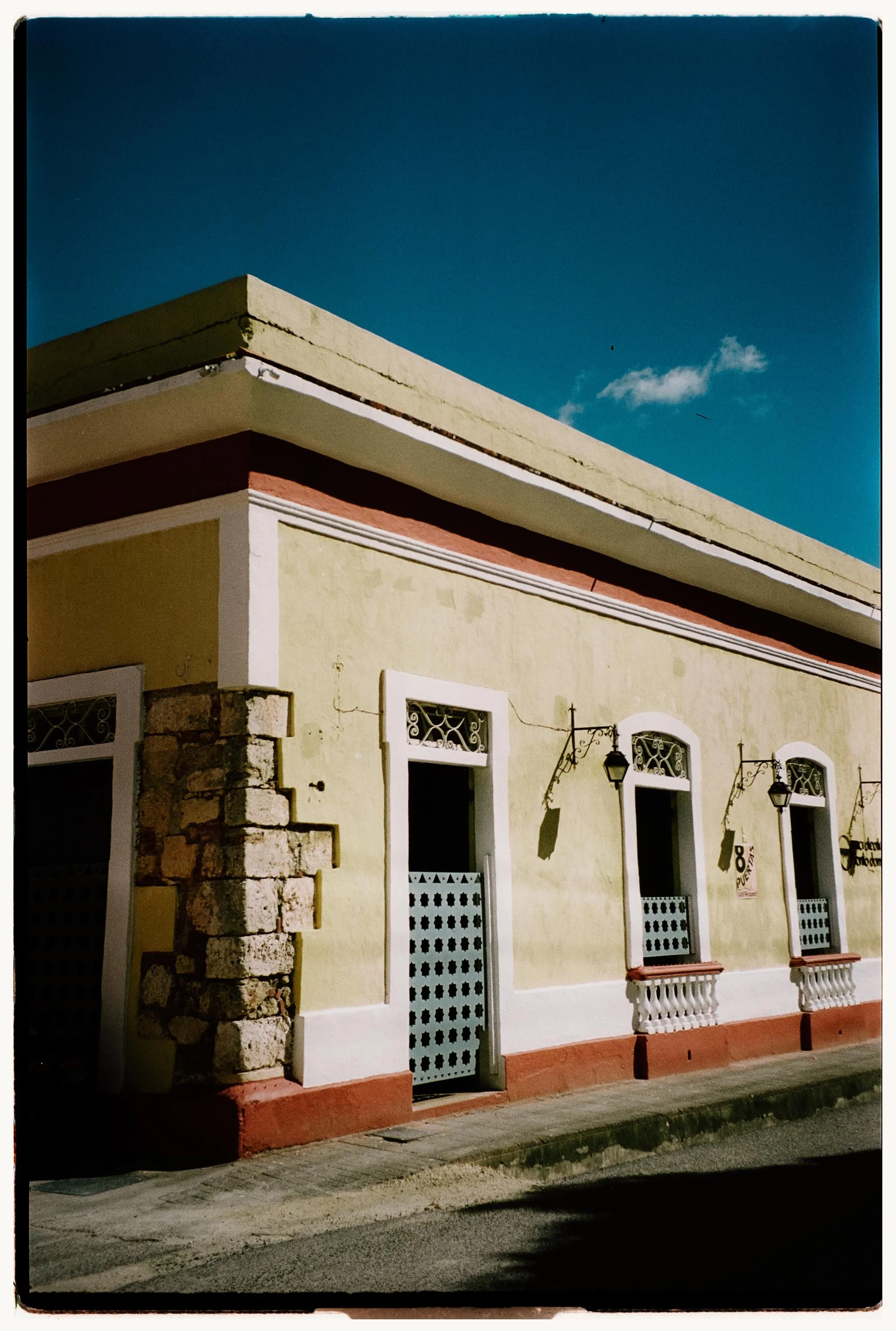 Corner of a yellow colonial building with red trim and exposed stone under a clear blue sky in Santo Domingo.