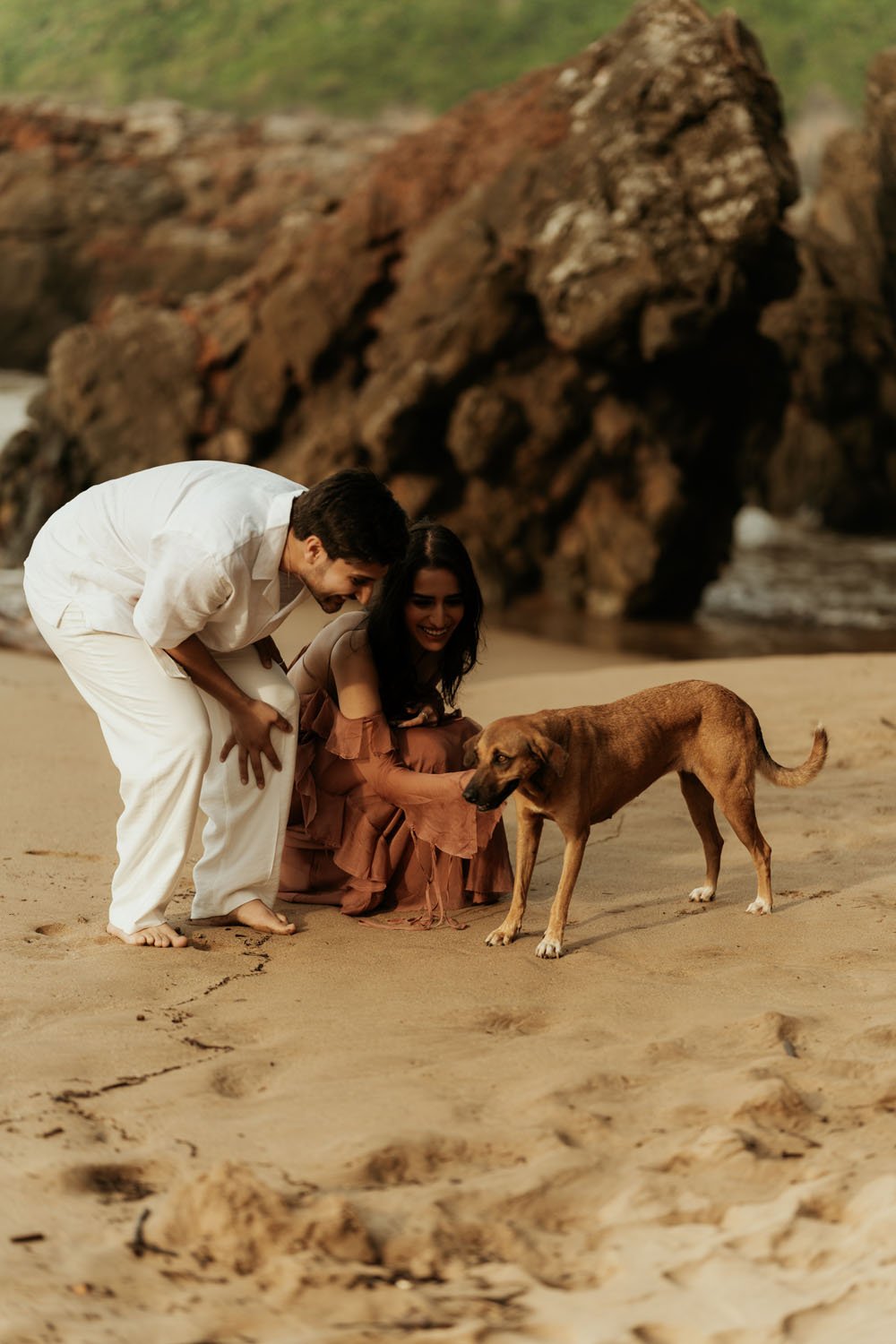 Candid engagement moment with couple petting a stray dog on the sand