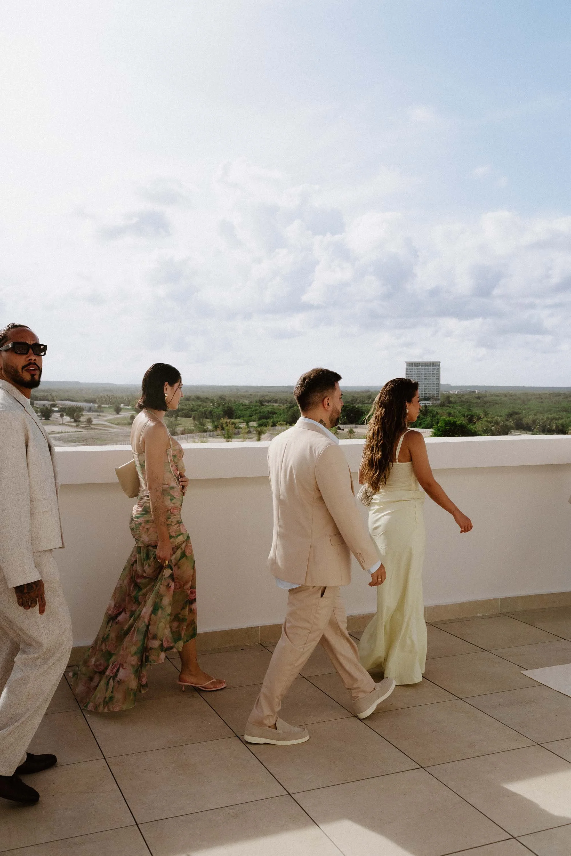 Candid, editorial photograph of stylish wedding guests in light pastel summer attire walking together along a sunlit terrace before the ceremony in Cap Cana Punta Cana