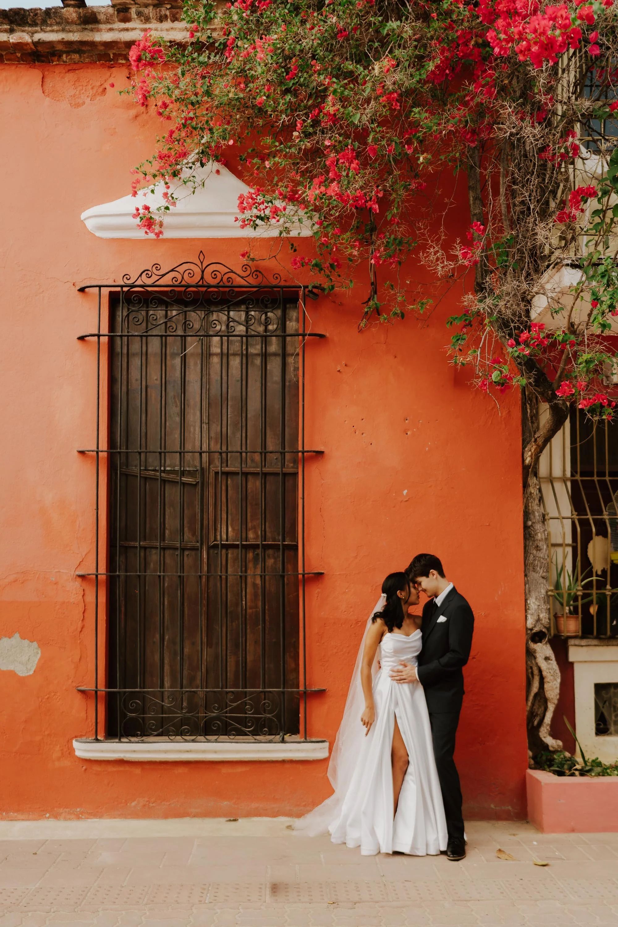 Bride and groom hugging in front of a terracotta colonial wall with bougainvillea flowers in the Zona Colonial.