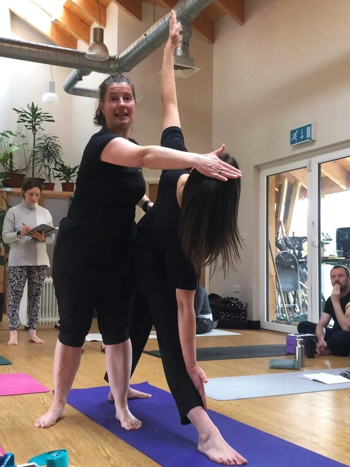 Yoga teacher demonstrating a hands-on adjustment in Triangle Pose during a workshop