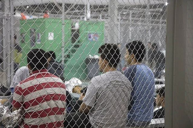 inside a detention center, people huddle behind chain link fencing