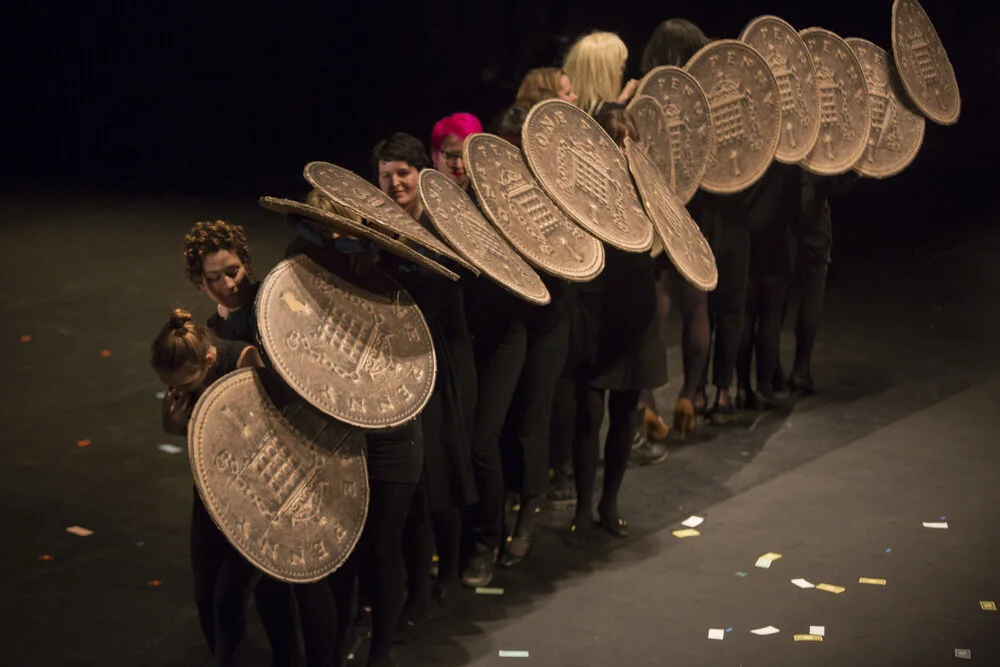 Line of performers holding shields in form of huge one penny coins