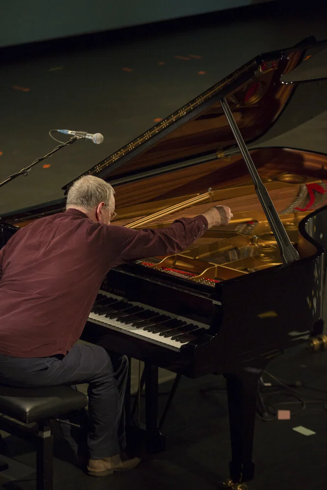 Pianist leans into and adjusts the innards of a grand piano