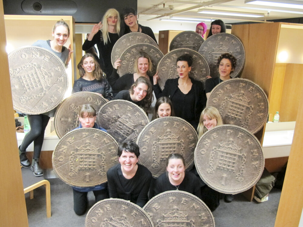 Performers smile at the viewer from behind their one penny coin shields backstage