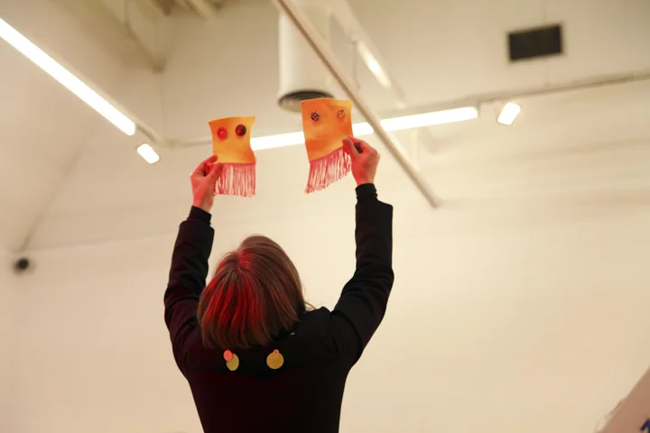Hayley Newman holds two squares of orange material with tassels above her head
