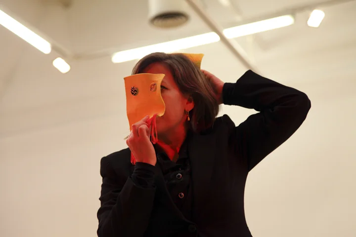 Hayley Newman holds a square piece of material in front of her face, two buttons suggest eyes