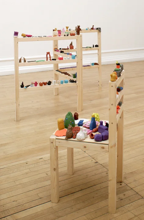 A wooden chair and shelves on which are perched many small brightly coloured plasticine objects