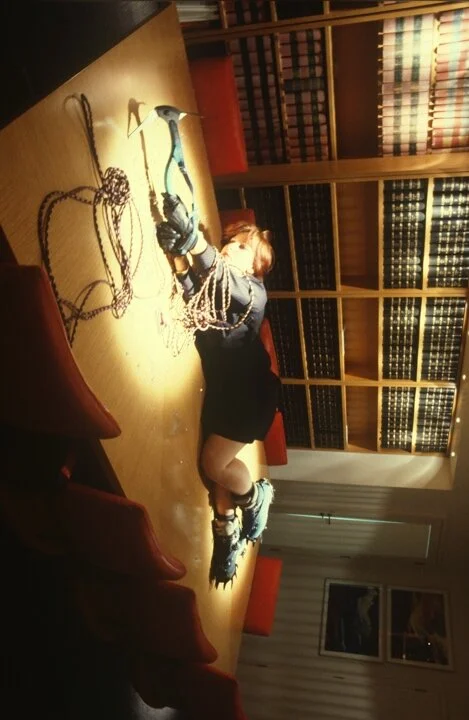 Hayley Newman, photographed vertically, lies on a boardroom table using mountaineering equipment