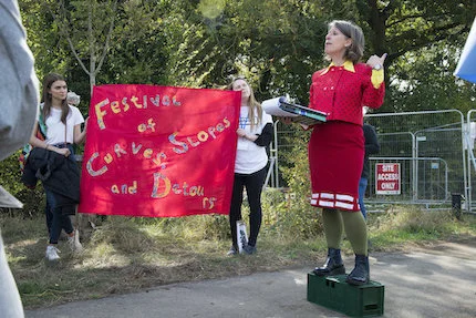 Hayley Newman in red dress addressing the group with banner in background with words - festival of curves, slopes and detours