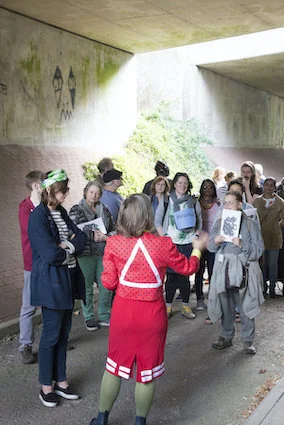 Hayley Newman in red dress with white triangle addressing group of people