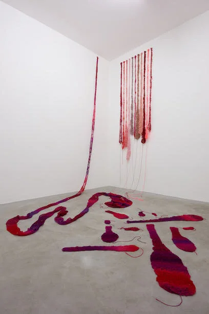 A gallery space with red knitted tongues on floor and walls