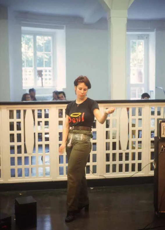 Hayley Newman playing air guitar, a microphone is taped to her waist and pointing downwards