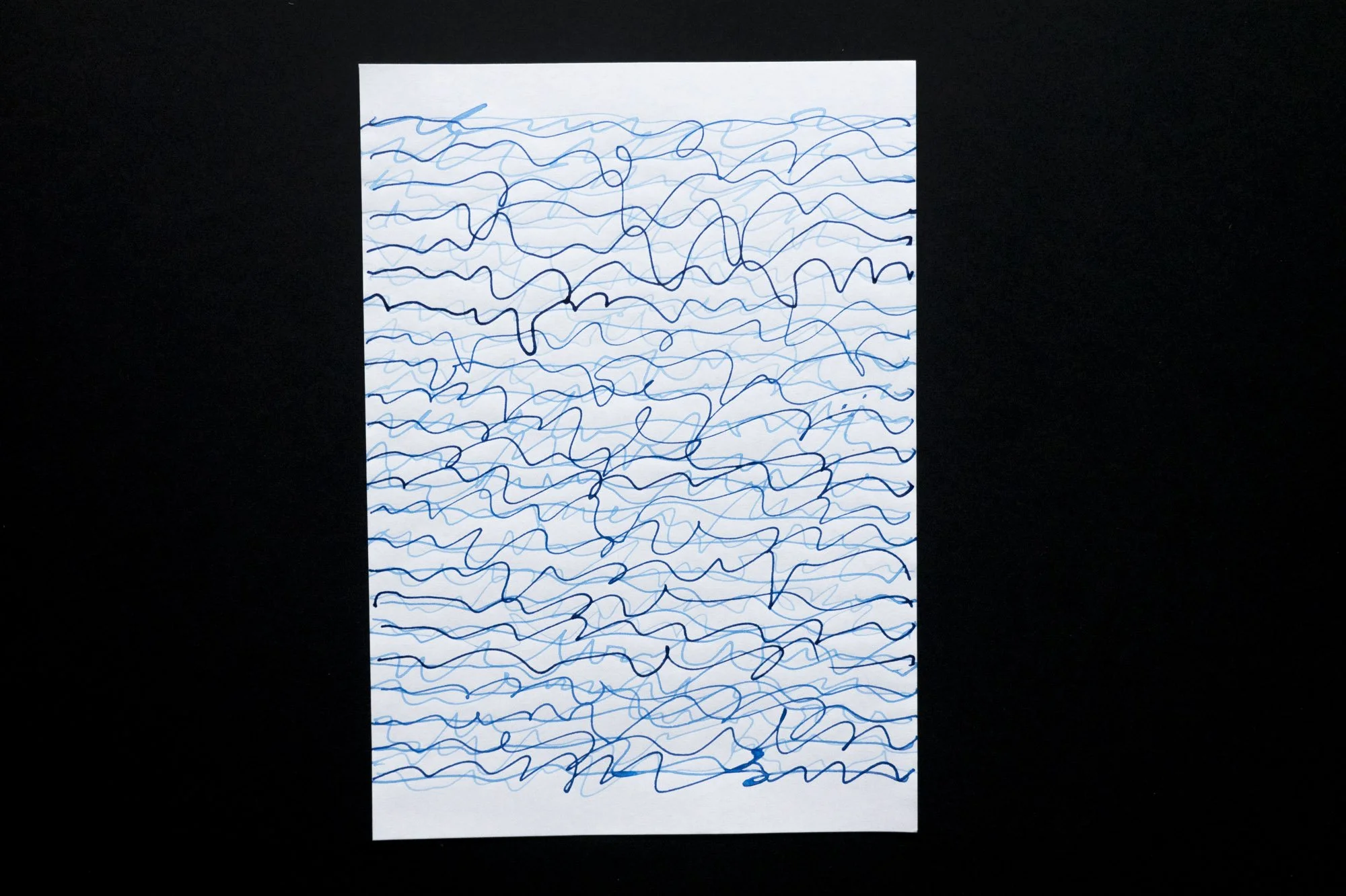 A white piece of paper on which irregular blue ink lines are drawn like handwriting