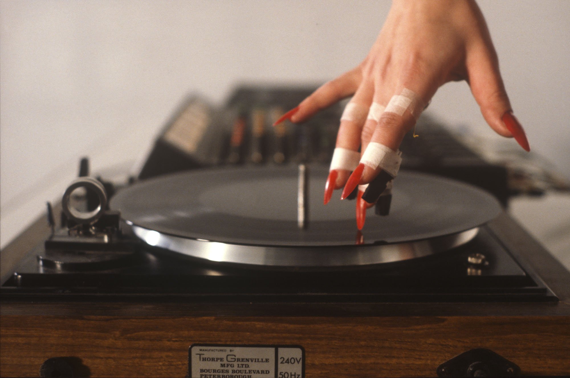 Close-up of Hayley Newman’s hand touching a record with the tip of a long red finger nail 