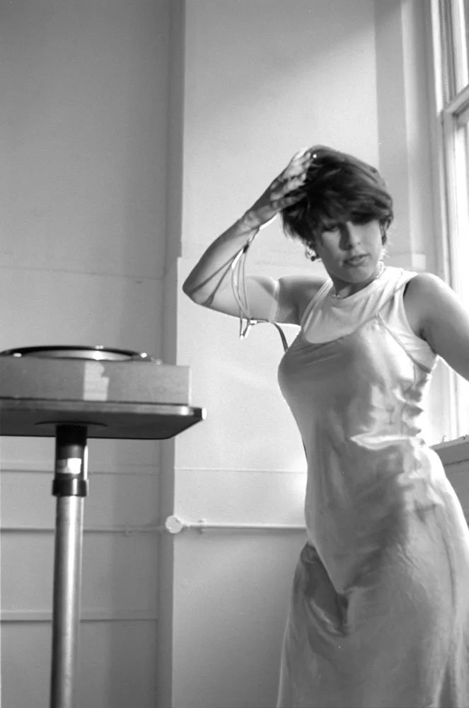 Hayley Newman gestures with wires attached to her right hand next to a record player