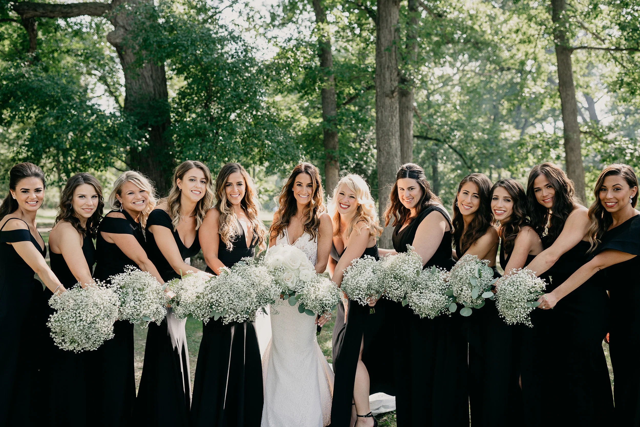 Bride with bridesmaids in black dresses holding white bouquets outdoors