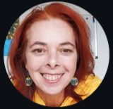 Close-up of a smiling woman with red hair, wearing earrings and a yellow top.