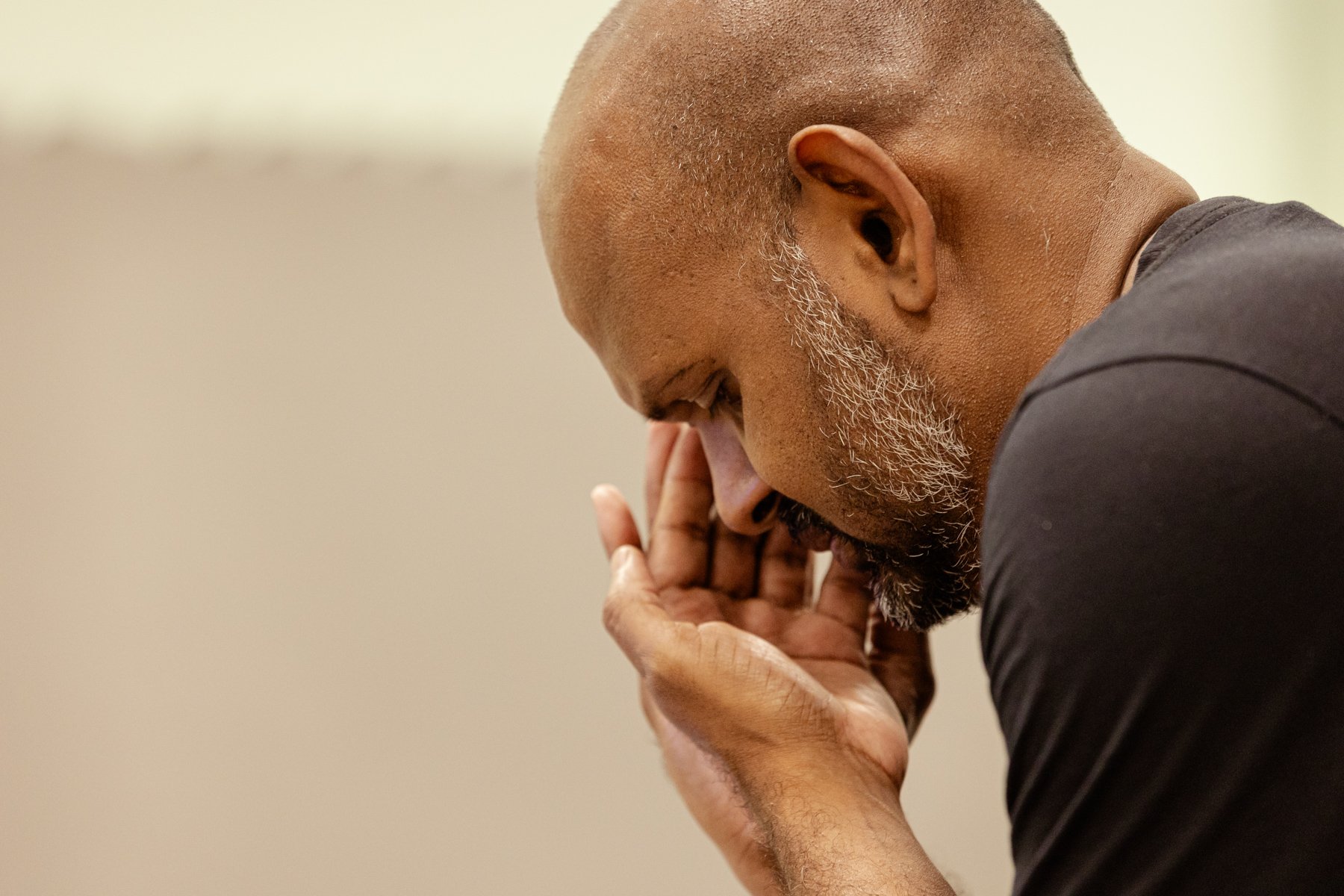  Photo of actor Ramesh Meyyappan in the rehearsal room. This is a close-up of Ramesh’s head and shoulders. He has his head bent down looking at his hands which are resting on top of each other, palms raised, close to his head. 