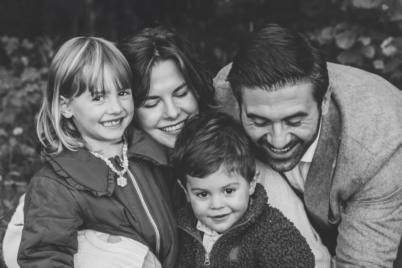 en familj med mamma, pappa, och två barn sitter utomhus och kramar om varandra. Alla är glada. Bilden är svartvit